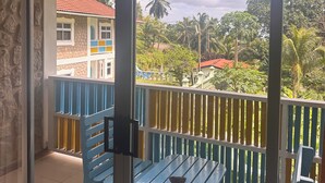 Ein Balkon mit blauen Stühlen und einem Tisch, mit Blick auf ein Gebäude mit rotem Dach und Palmen.