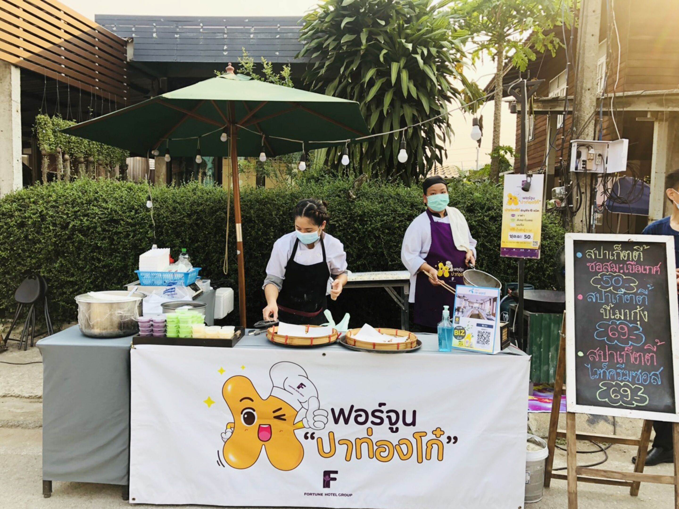 A street food stall with a table covered in food items and a sign with Thai text.
