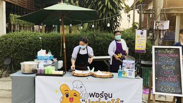 A street food stall with a table covered in food items and a sign with Thai text.
