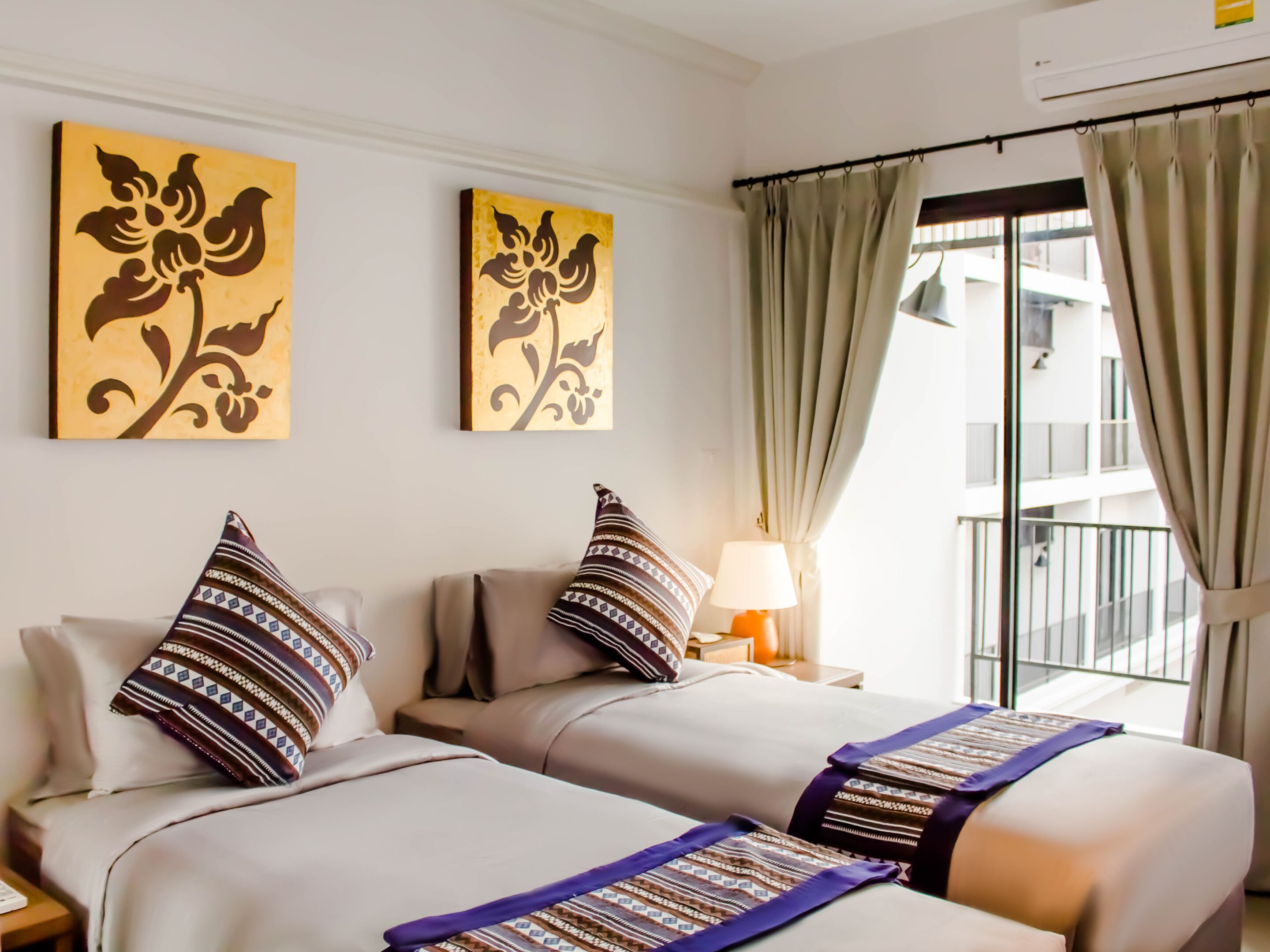 Une chambre d’hôtel avec deux lits, une table de chevet avec une lampe et deux tableaux floraux accrochés au mur.