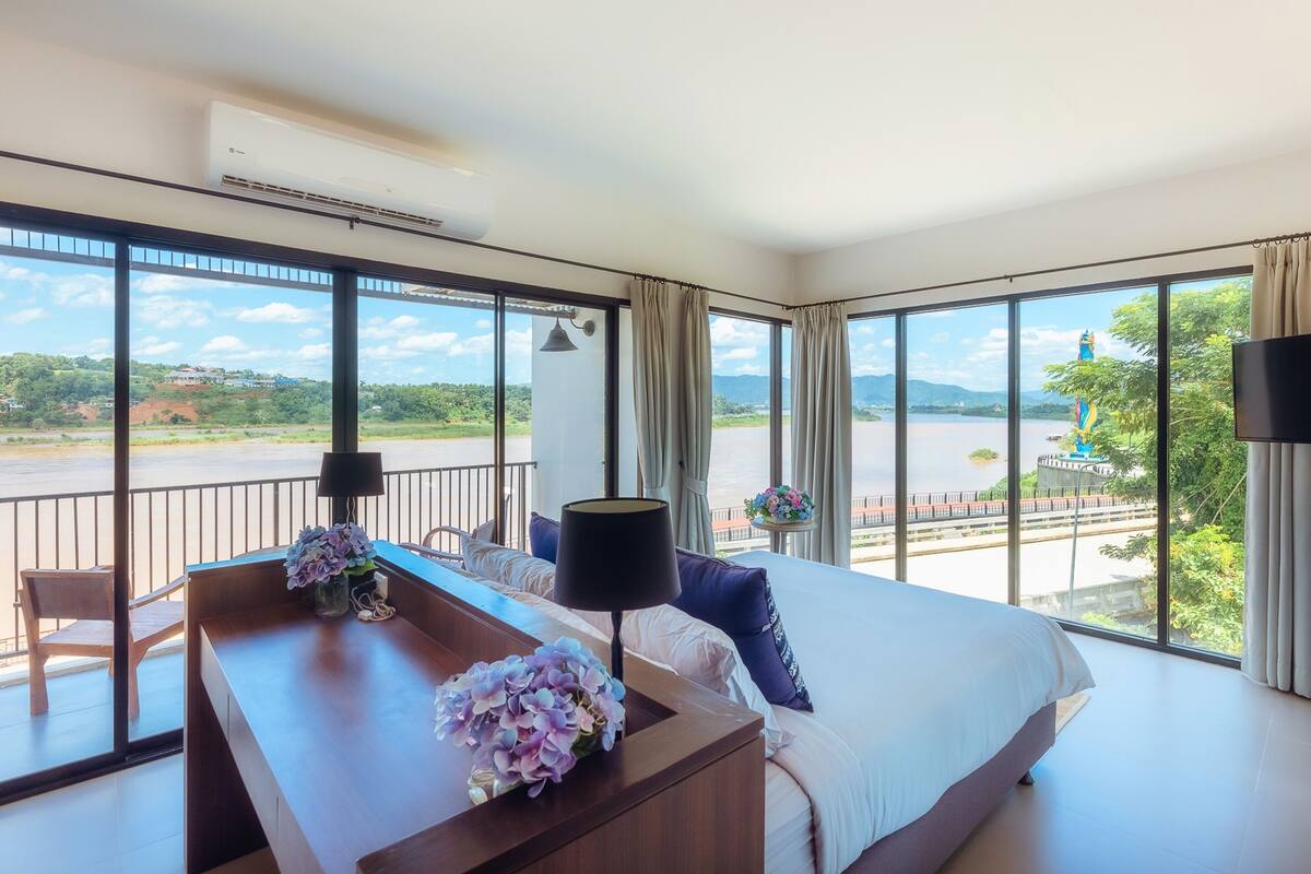 Habitación de hotel con una cama grande, un escritorio, una silla y vistas a un río y montañas.