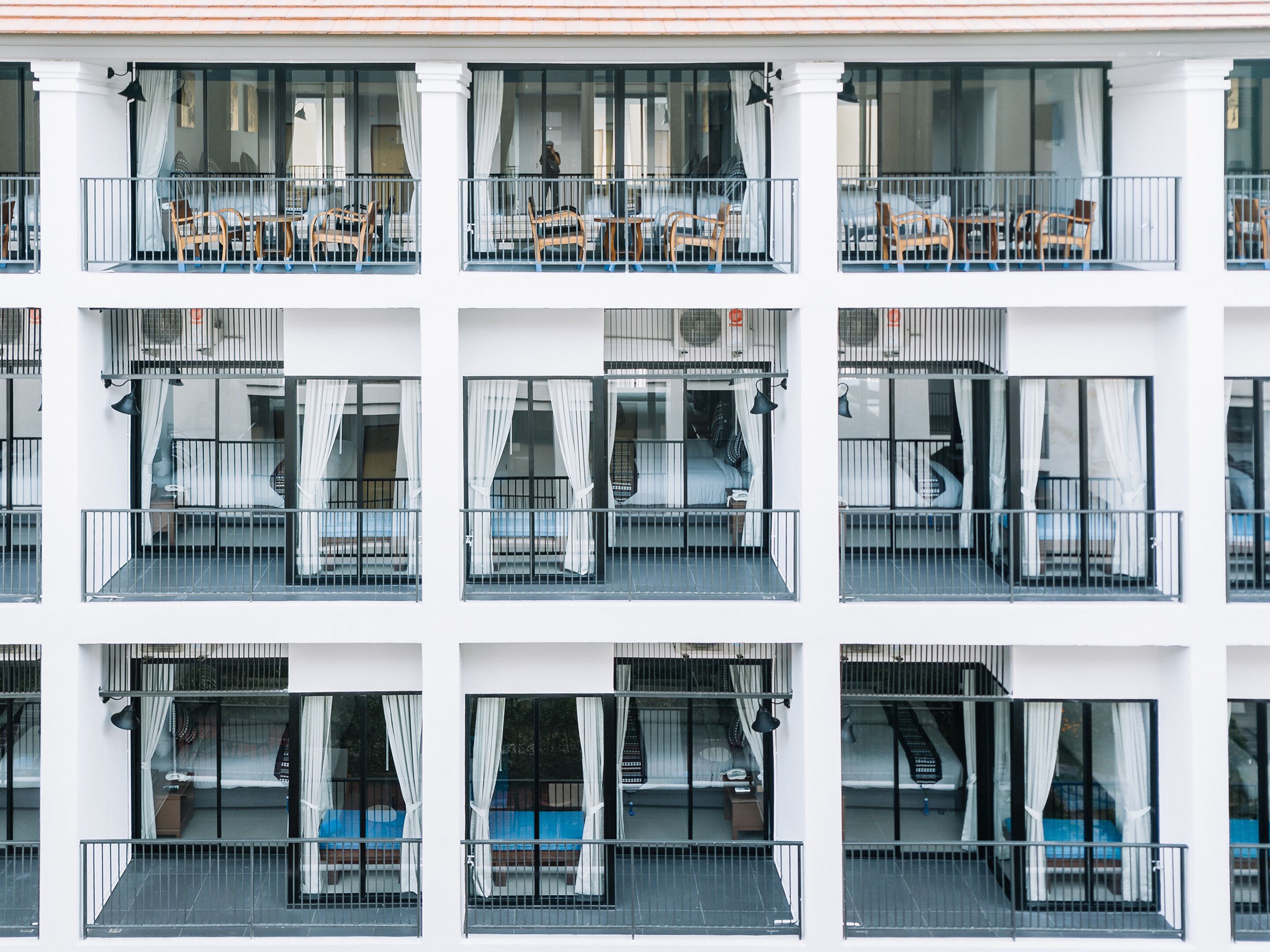 Un hotel de varios pisos con balcones, cada uno con una cama y una mesita.