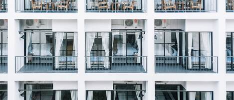 Un hotel de varios pisos con balcones, cada uno con una cama y una mesita.