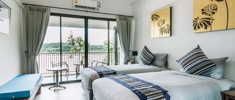 A hotel room with two beds, a balcony with a table and chairs, and artwork on the walls.