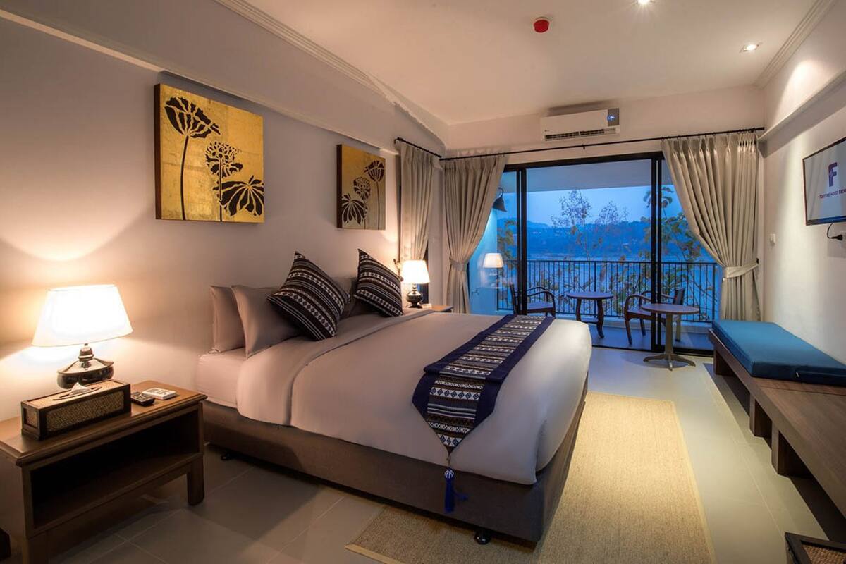 Habitación de hotel con cama, mesitas de noche, escritorio y balcón con vistas.
