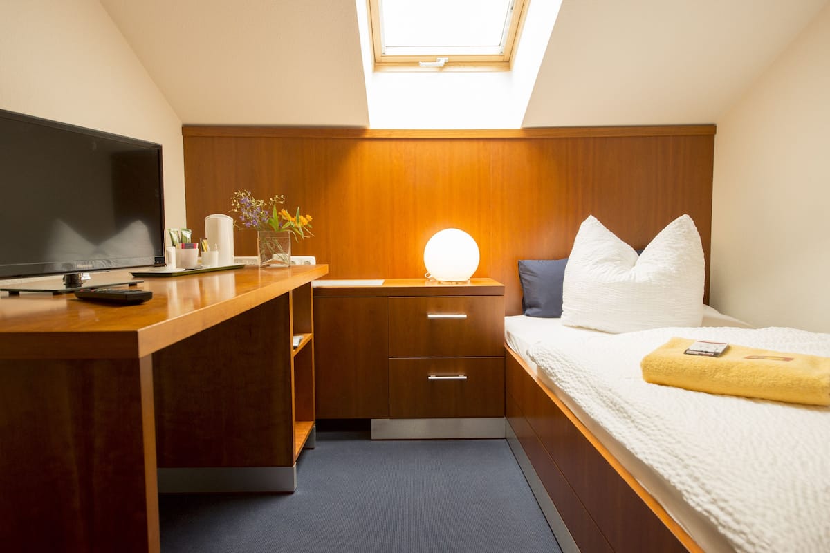 A compact hotel room with a bed, bedside table, TV, and a skylight.