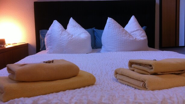 A neatly made bed with white pillows and folded towels. - Pension Freiraum Guesthouse Berlin (Berlin)