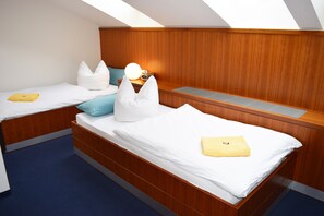 A compact room with two beds, each with a pillow and a folded towel. There is a bedside table with a lamp and a radio. The room has wooden paneling on the walls and a sloped ceiling. - Pension Freiraum Guesthouse Berlin (Berlin)