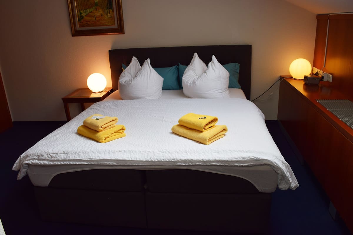 A neatly made bed with white bedding and two yellow towels, a dark headboard, teal pillows, and bedside lamps.