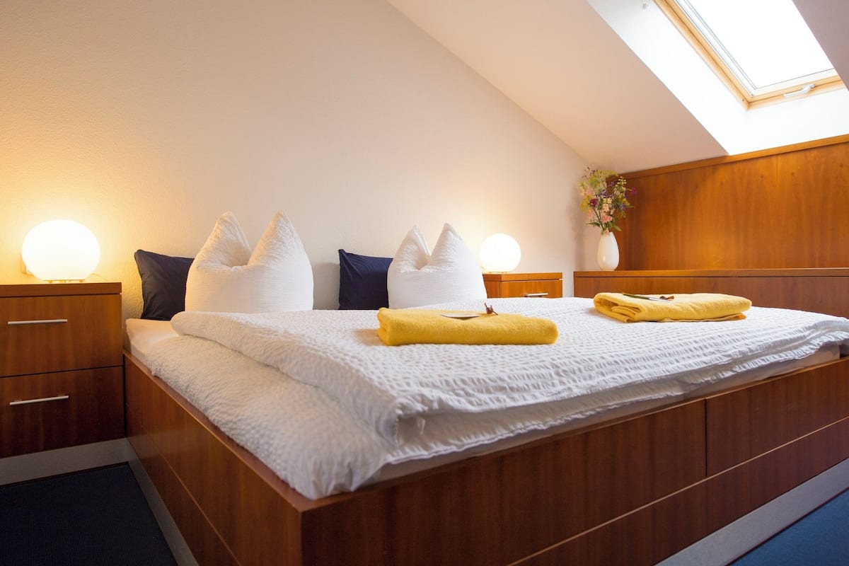 A bedroom with a large bed, wooden headboard, bedside tables with lamps, and a skylight.