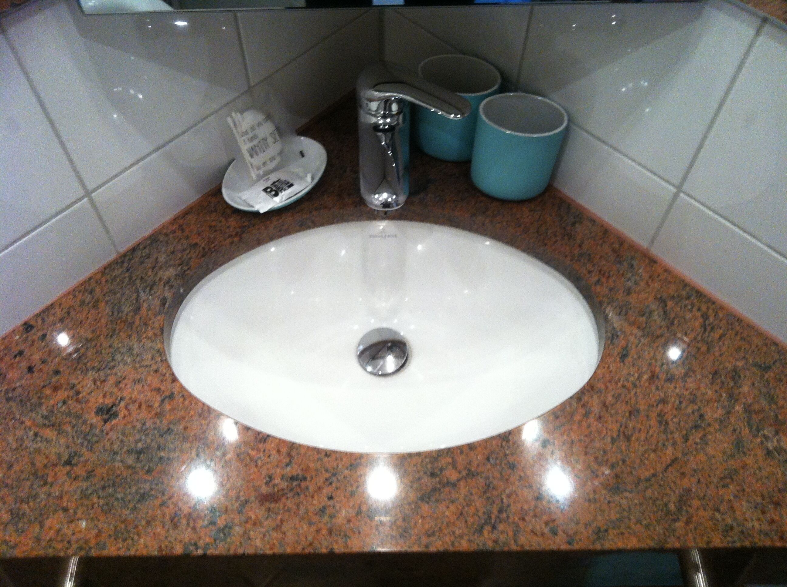 Un lavabo de salle de bain avec un plan de toilette en granit, un robinet et deux tasses bleues.