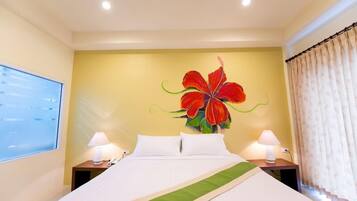 A hotel room with a bed, two bedside tables with lamps, a large floral artwork on the wall, and a window with curtains.