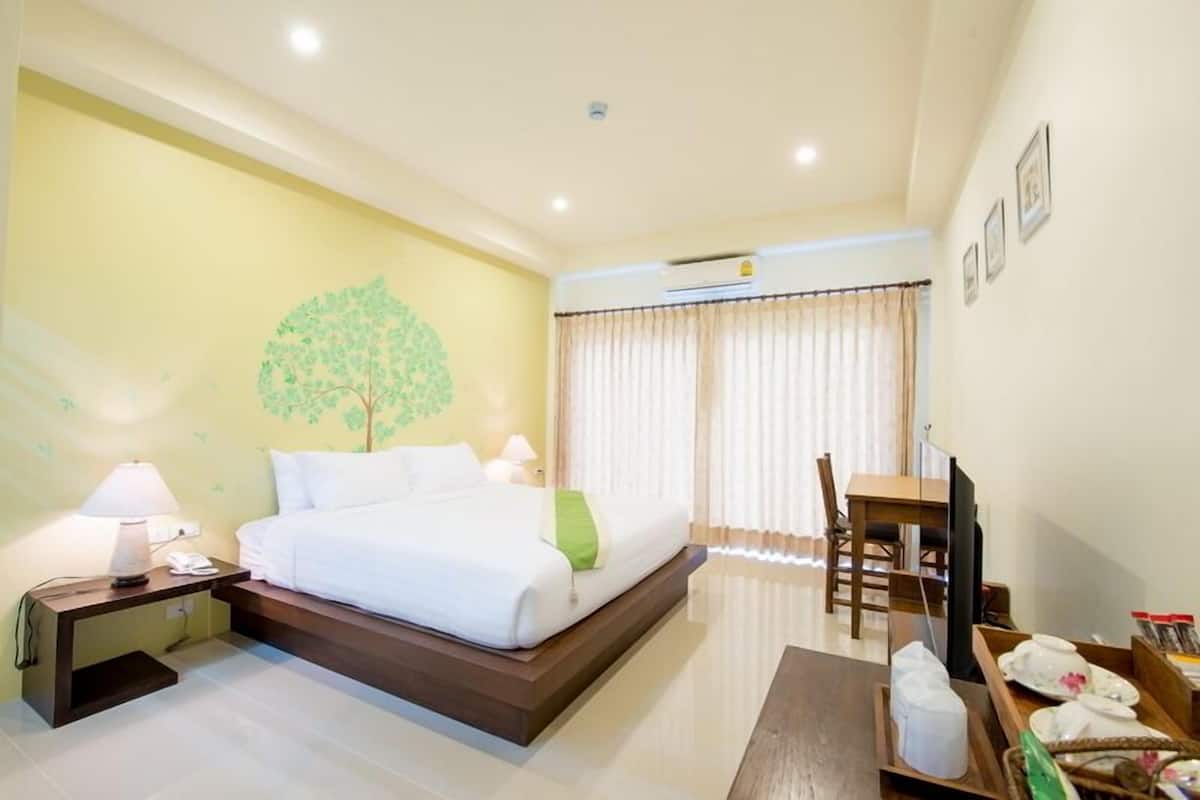 A hotel room with a bed, bedside table, lamp, TV, and a dining area with a table and chairs.