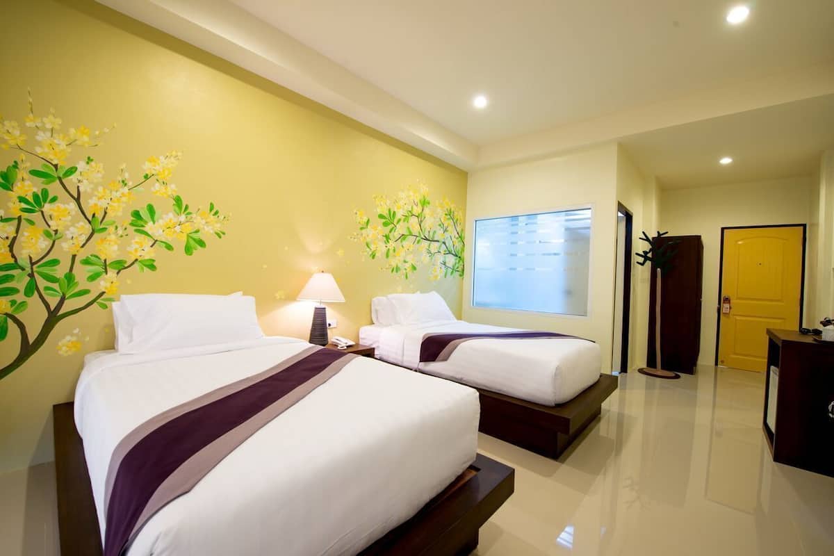 A hotel room with two beds, a window, a door, and a wall with a floral mural.