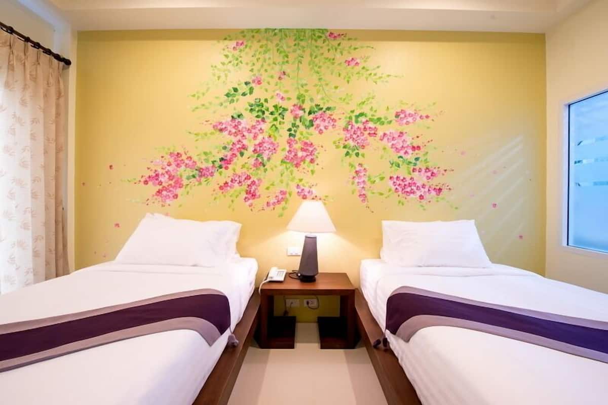 A hotel room with two beds, a nightstand with a lamp, and a wall mural of pink flowers.