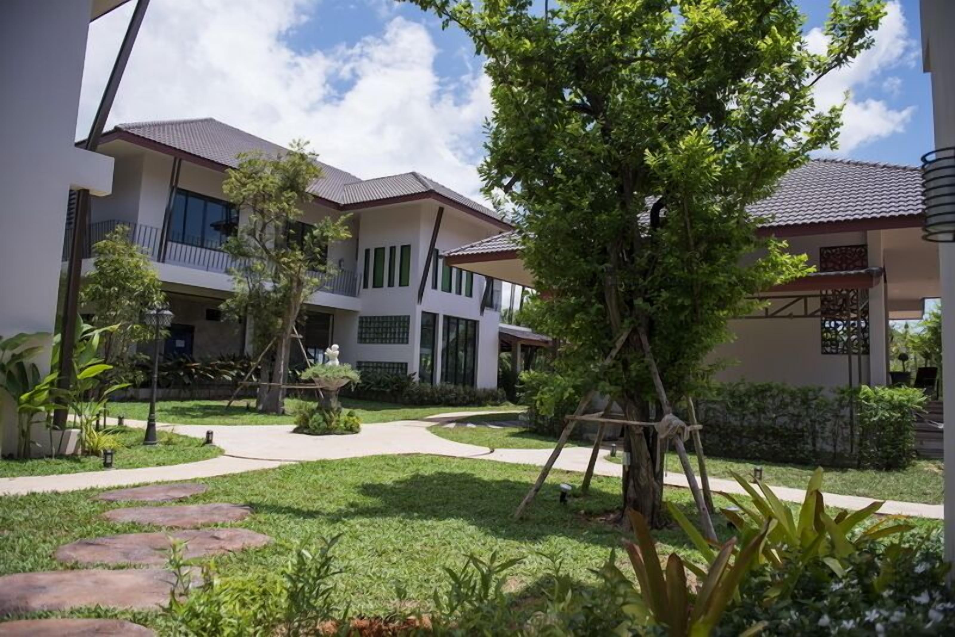A modern building with a garden courtyard, featuring a pathway, a swing set, and a variety of plants.