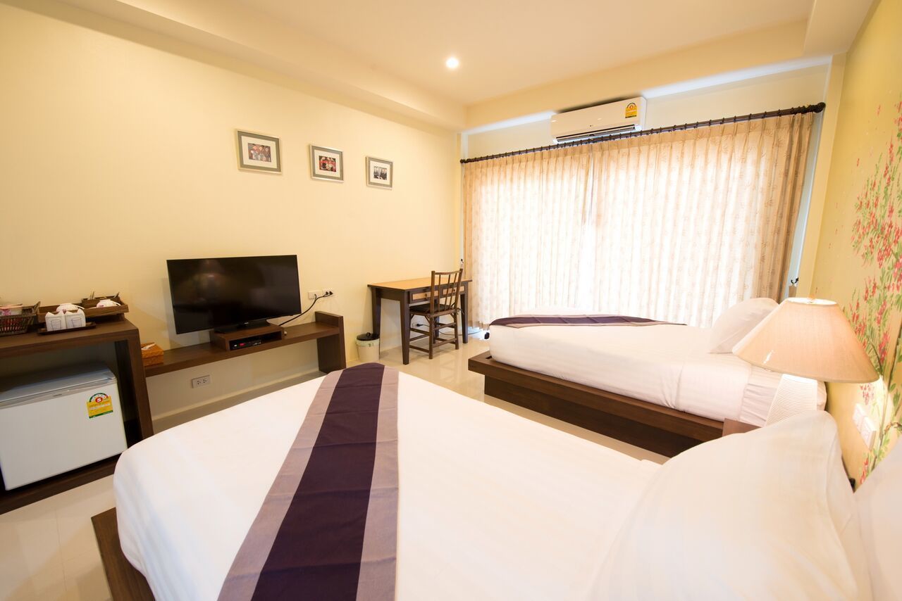 Een hotelkamer met een bed, een televisie op een bureau, een stoel en een raam met gordijnen.