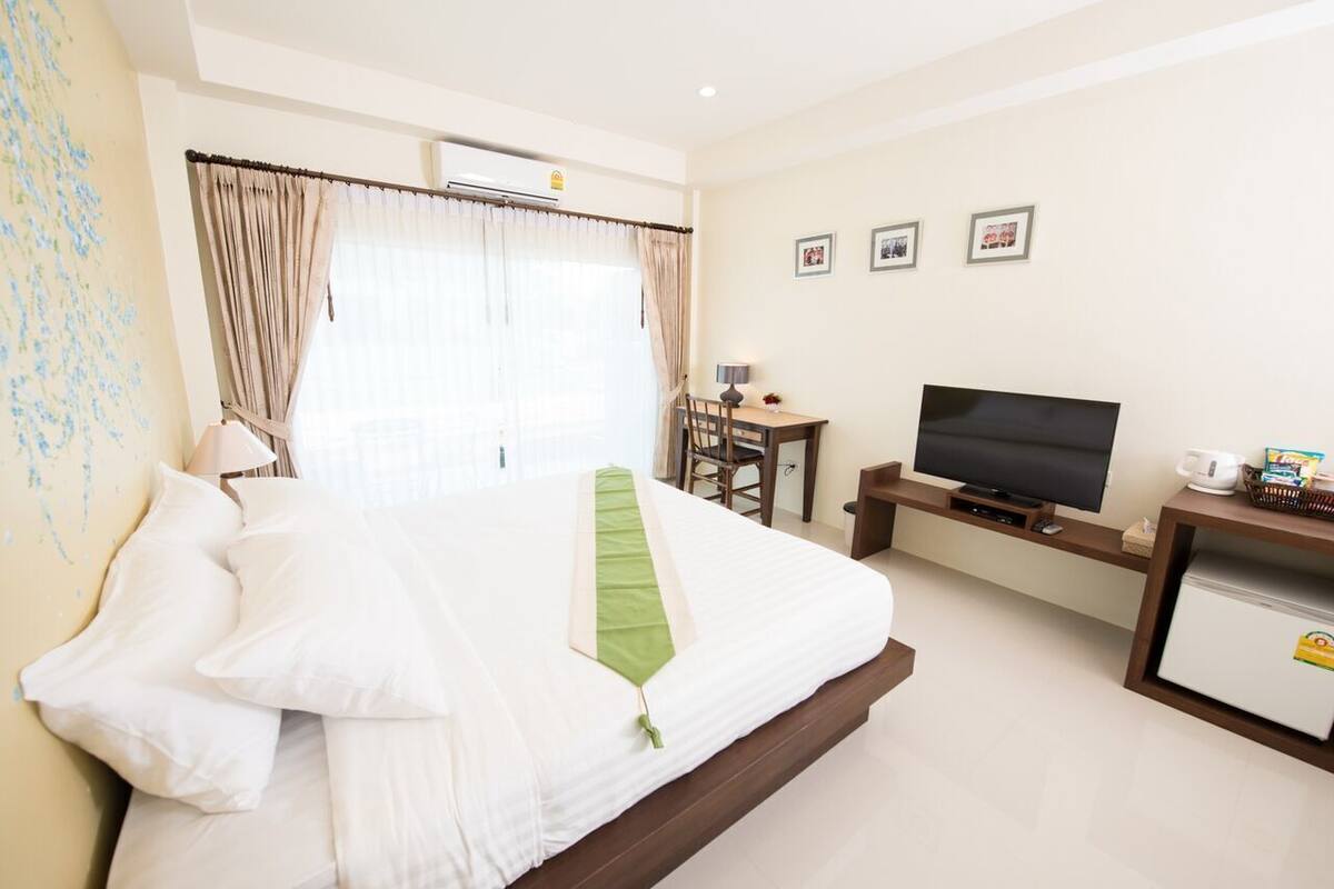 A hotel room with a bed, a TV, a desk with a chair, and a small refrigerator.