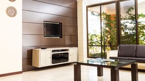 A modern living room with a flat-screen TV mounted on a wooden panel wall, a glass coffee table, and a sofa. - Hotel Ilhasul (Florianópolis)