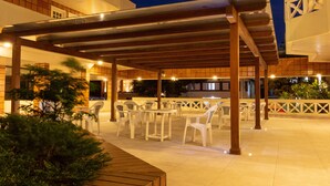 An outdoor patio area with tables and chairs, a wooden pergola, and a tiled floor. - Hotel Ilhasul (Florianópolis)