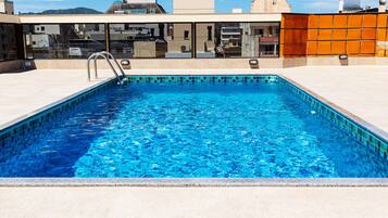 Et rektangulært swimmingpool med klart blåt vand, omgivet af en fliseterrasse.