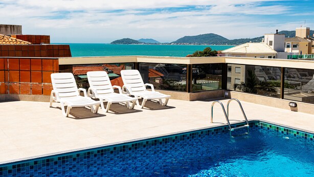 A rooftop pool with white lounge chairs and a view of the sea. - Hotel Ilhasul (Florianópolis)