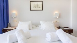 Un lit bien fait, avec du linge de lit blanc, deux tables de chevet avec des lampes et un tableau encadré au mur.