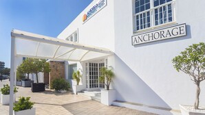 L’entrée d’un hôtel, avec un patio couvert, des plantes en pot et une enseigne indiquant « ANCHORAGE ».