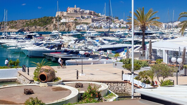 Un port de plaisance avec des bateaux amarrés, un sentier pavé et, au fond, un bâtiment avec un toit rouge.