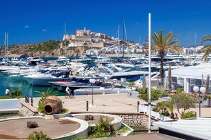 A marina with boats docked, a stone pathway, and a building with a red roof in the background. - Anchorage (Ibiza Town)