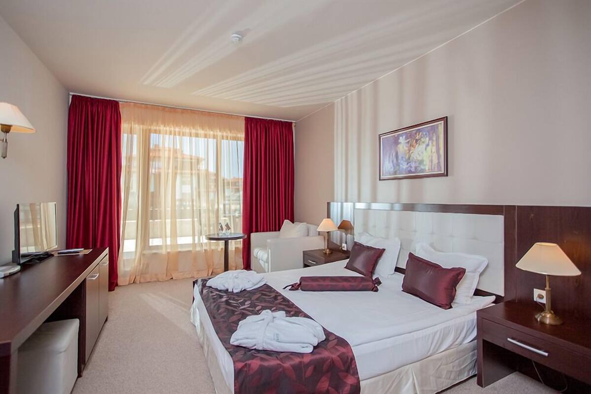 Ein Hotelzimmer mit einem großen Bett, einem Schreibtisch, einem Sessel, einem kleinen Tisch und einem Bild an der Wand.