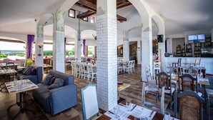 A spacious restaurant with high ceilings, white brick pillars, and a mix of seating arrangements including tables and chairs.