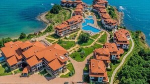 A coastal resort with multiple buildings, a central swimming pool, and a view of the sea.