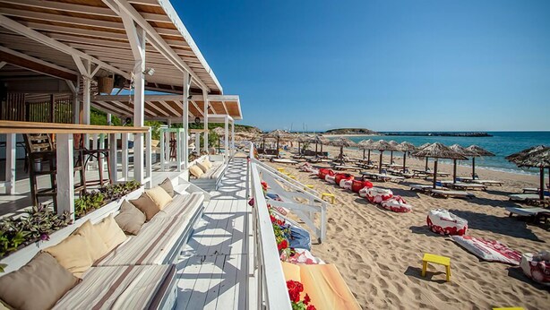 A beachside hotel with a wooden deck, beach chairs, umbrellas, and a clear view of the sea.