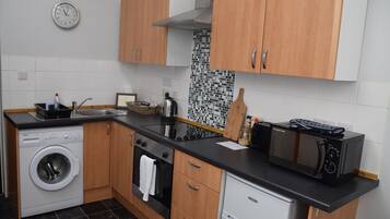A compact kitchen with wooden cabinets, a washing machine, a microwave, and a kettle.
