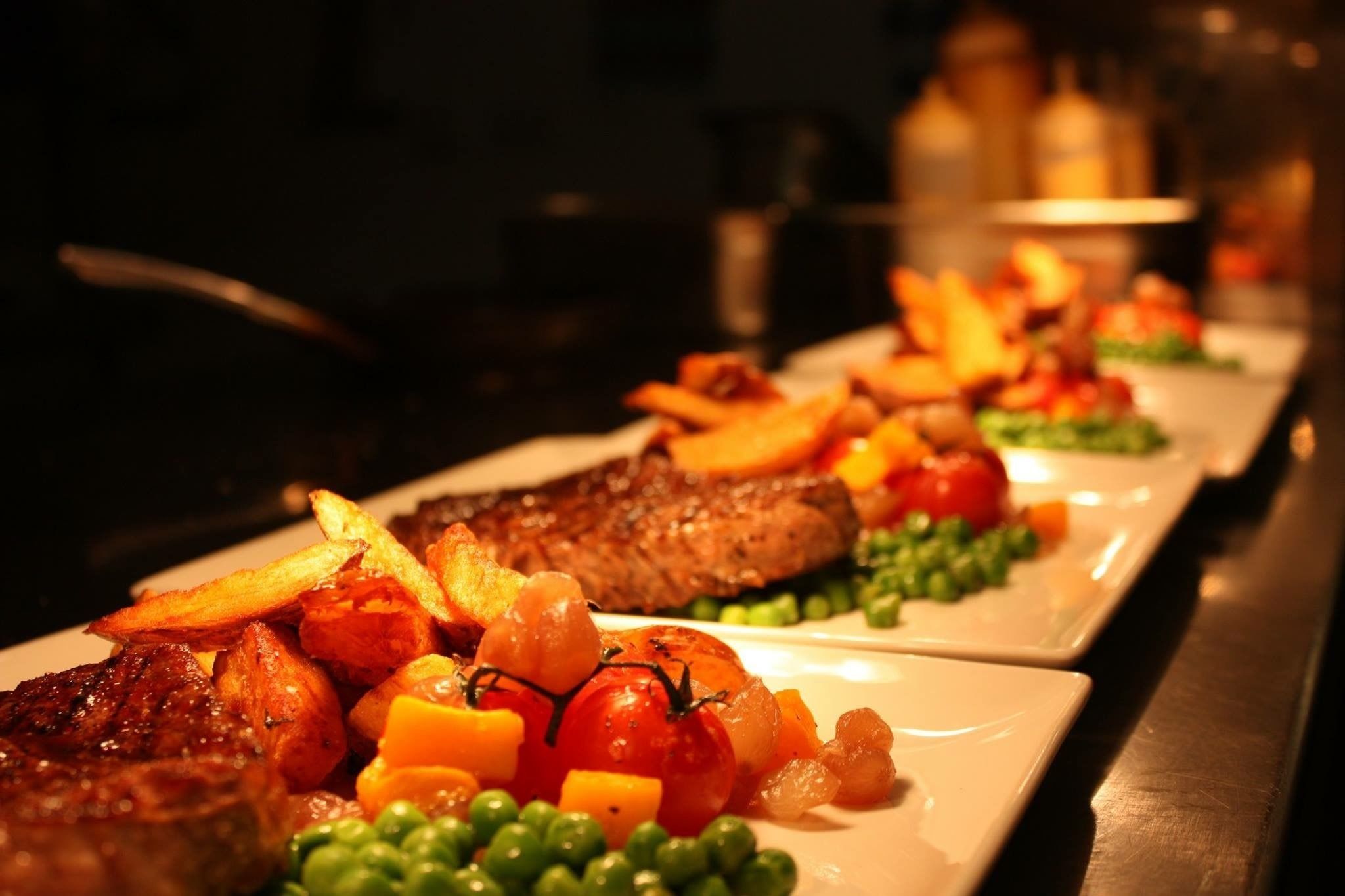 A row of plates with steak, vegetables, and potatoes.