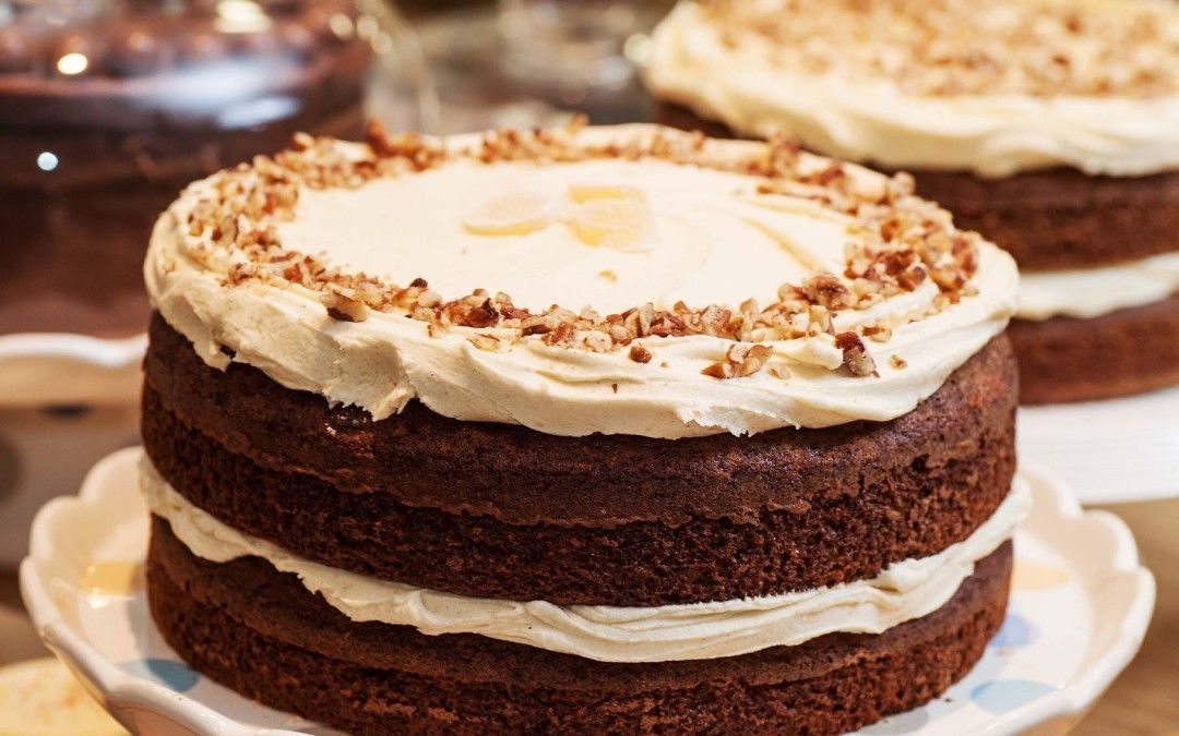 Un pastel con varias capas, cobertura blanca y nueces picadas por encima.