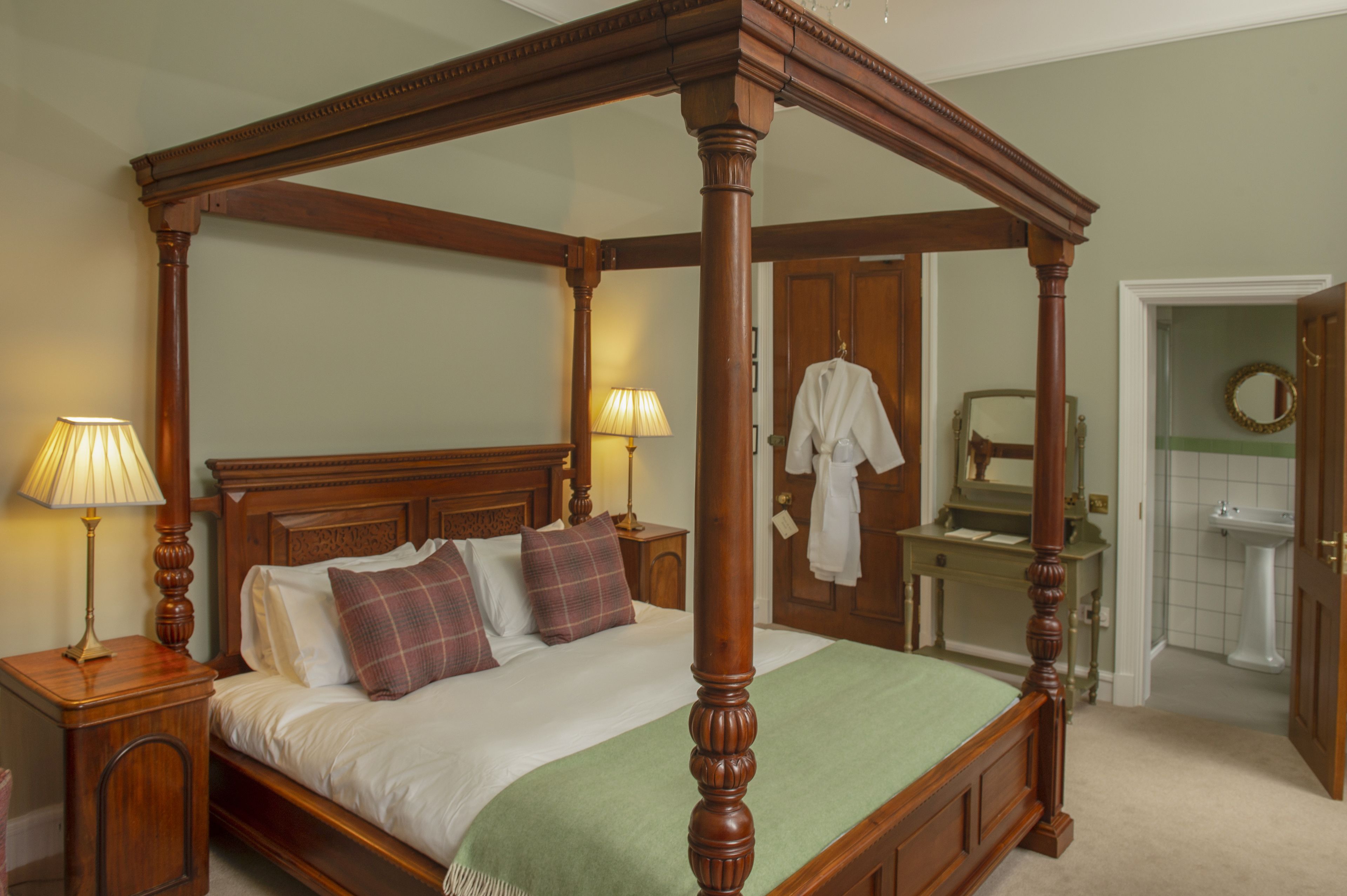 Un lit à baldaquin avec une couvre-lit verte, deux lampes de chevet et une table de chevet en bois.