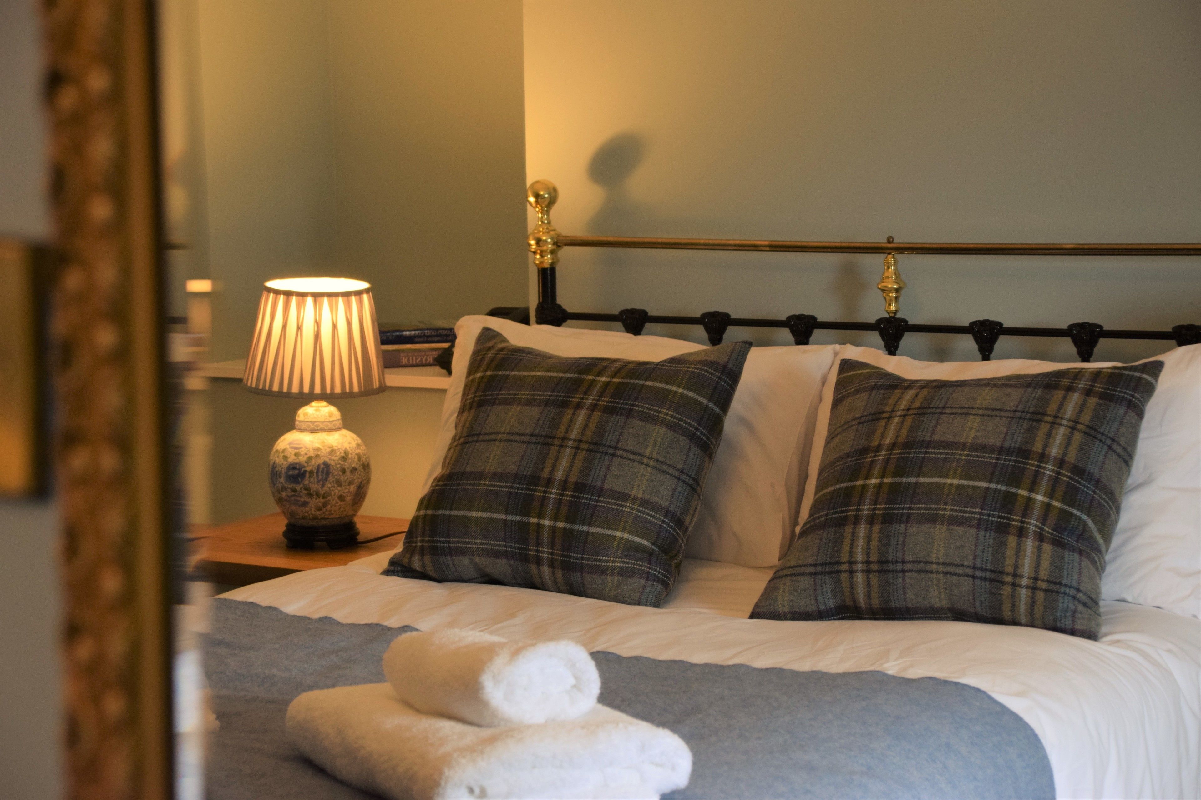 A neatly made bed with plaid pillows, a bedside lamp, and a rolled towel on the bed.