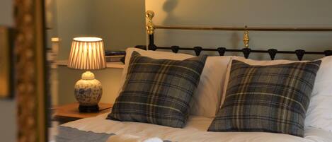 A neatly made bed with plaid pillows, a bedside lamp, and a rolled towel on the bed.