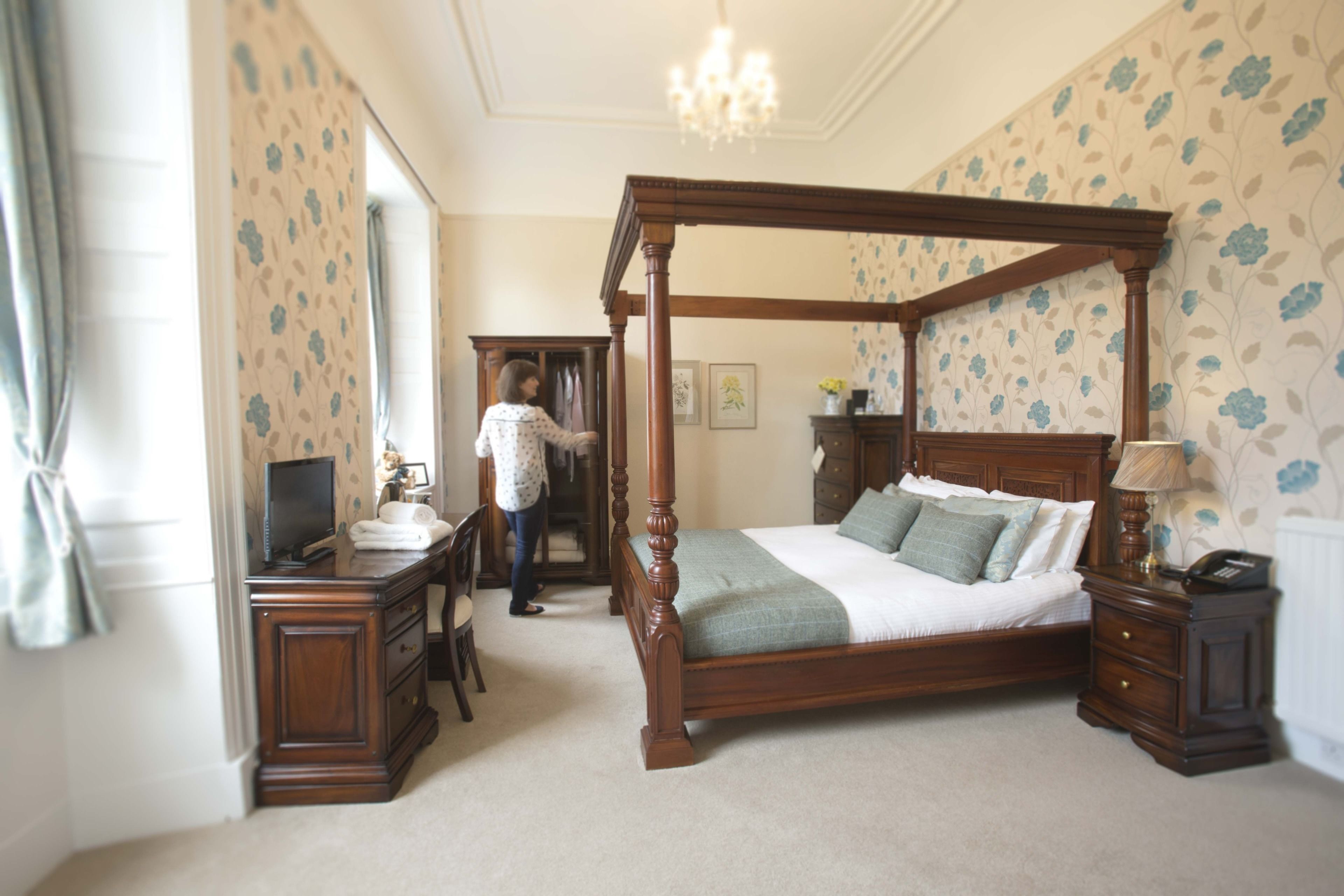 A bedroom with a four-poster bed, a desk with a computer, and a dresser.