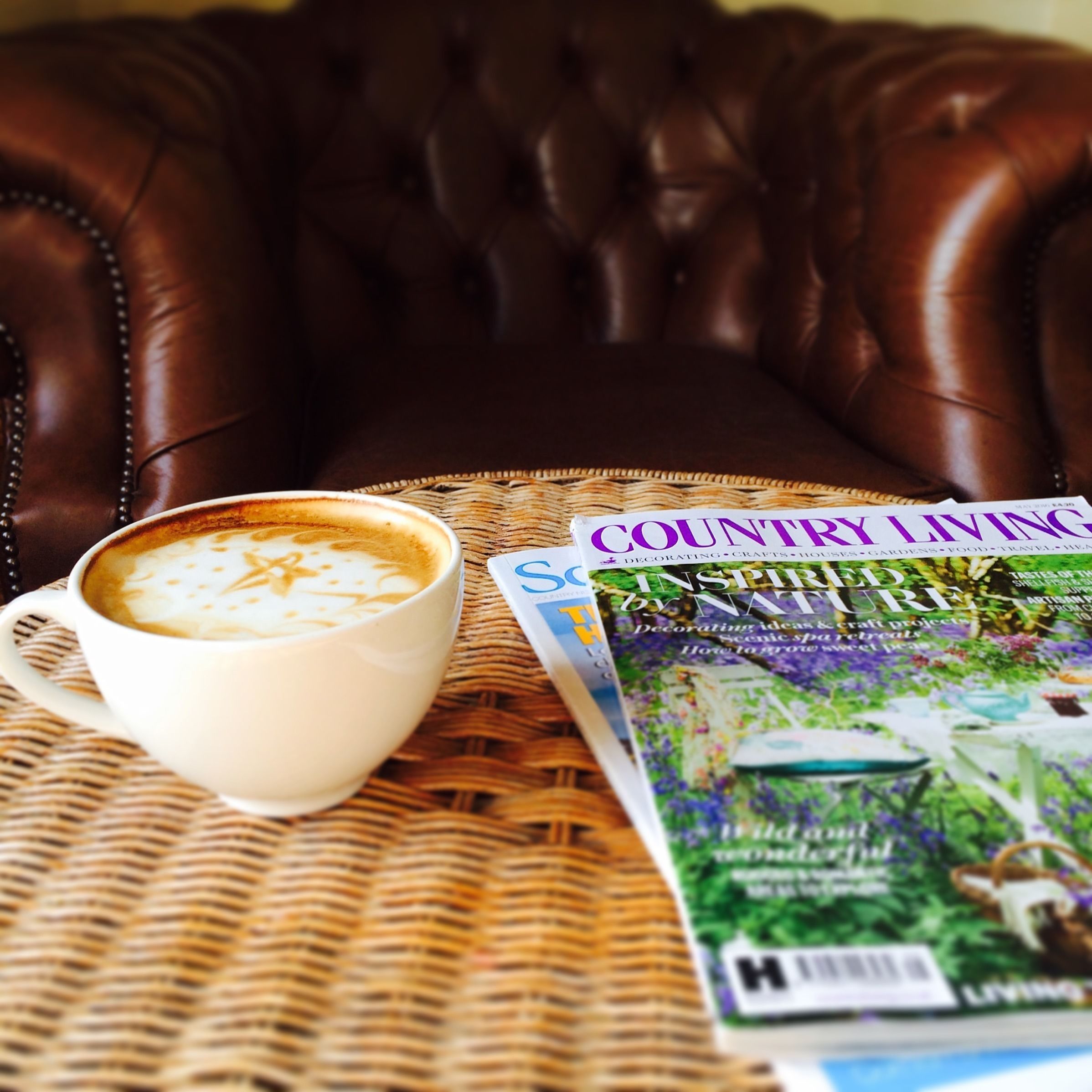 En kop kaffe på et fletbord med et magasin med titlen "Country Living" og et andet magasin.
