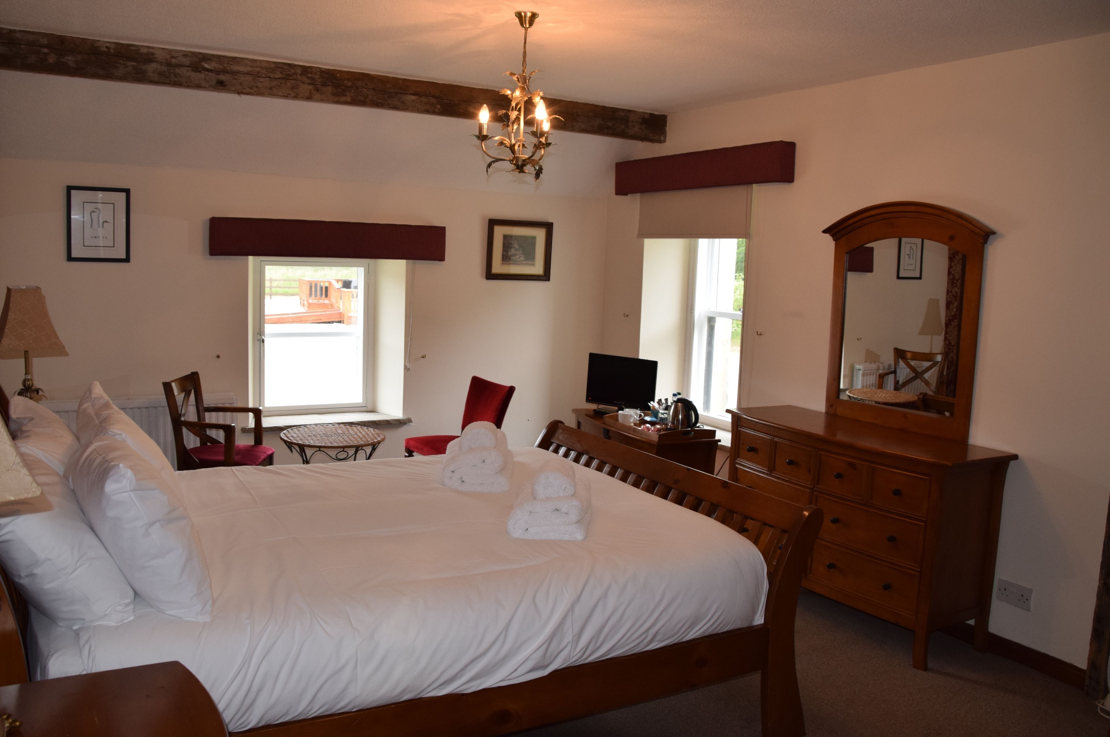 A neatly made bed with white linens and towels, a wooden dresser, a desk with a computer, and a chandelier.