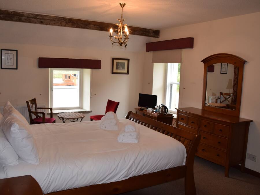 A neatly made bed with white linens and towels, a wooden dresser, a desk with a computer, and a chandelier.