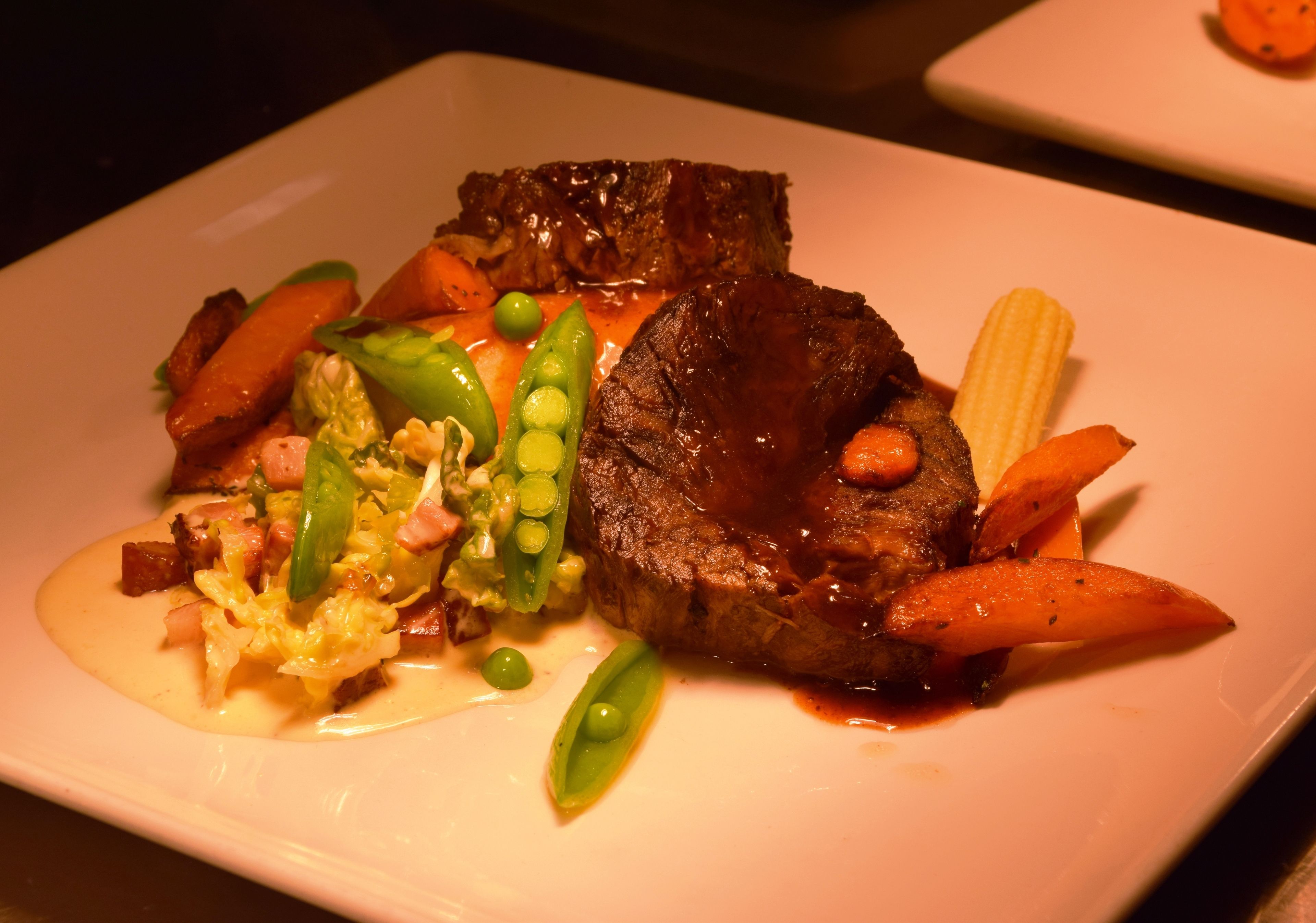 Une assiette contenant un steak, des carottes, des petits pois et un épi de maïs.