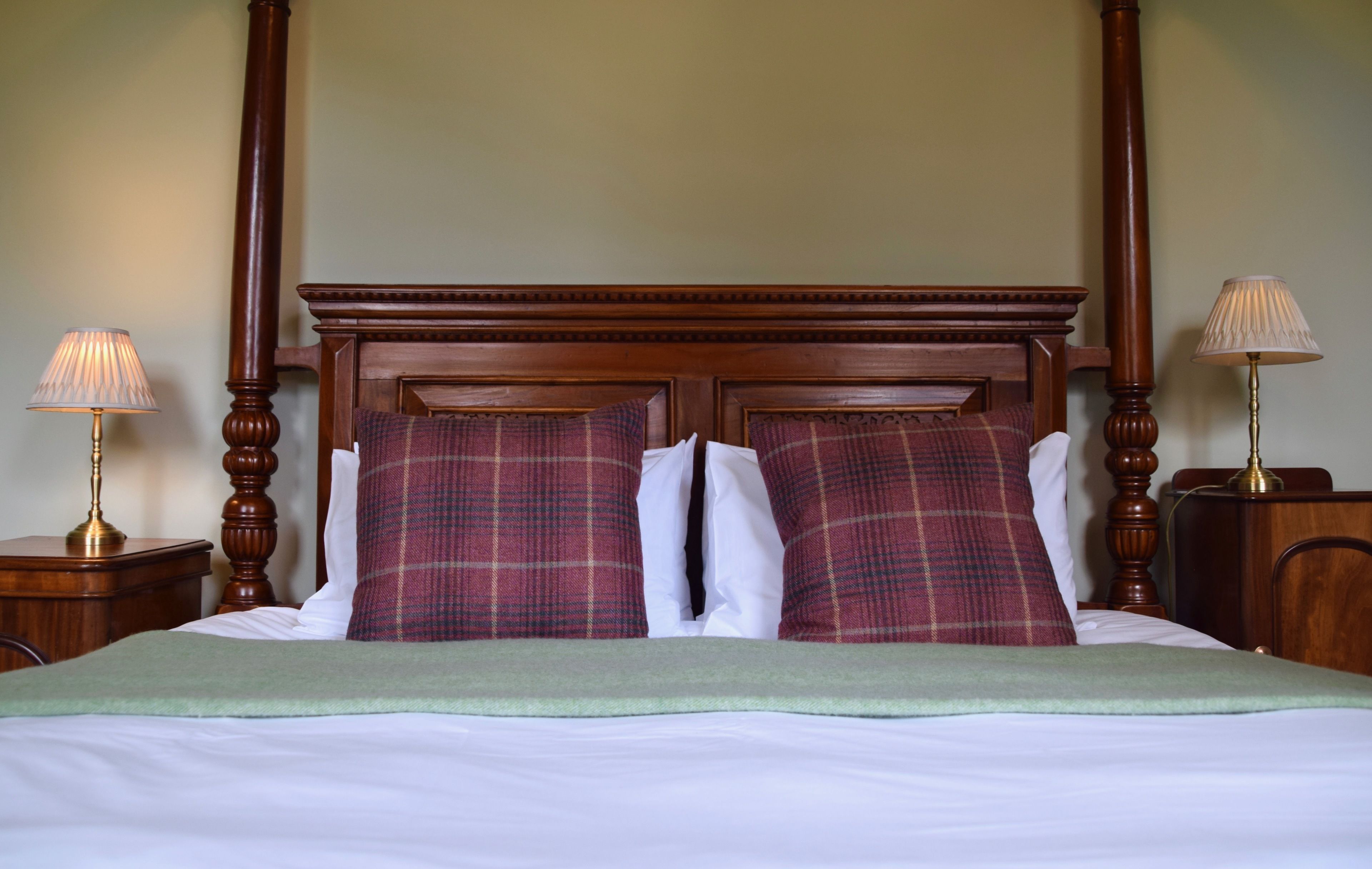 A four-poster bed with plaid pillows, a green throw blanket, and two bedside lamps.