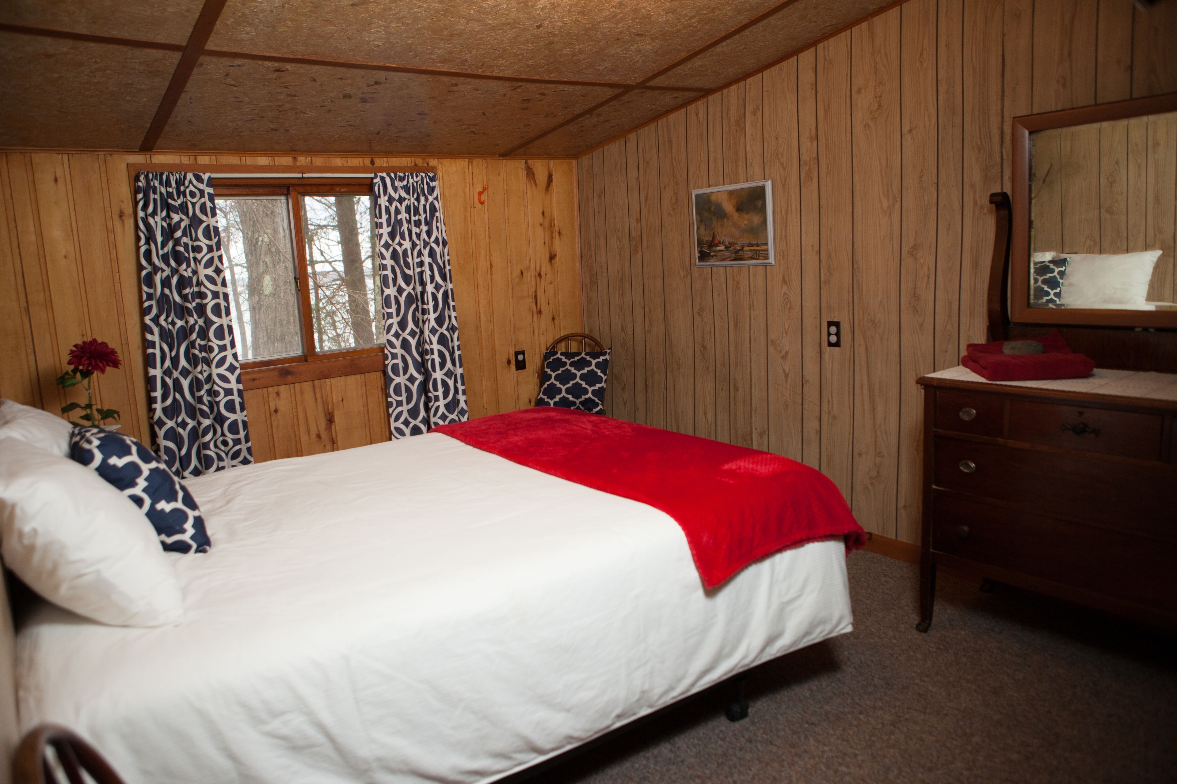 A wooden-paneled room with a bed, a dresser, and a window with curtains.