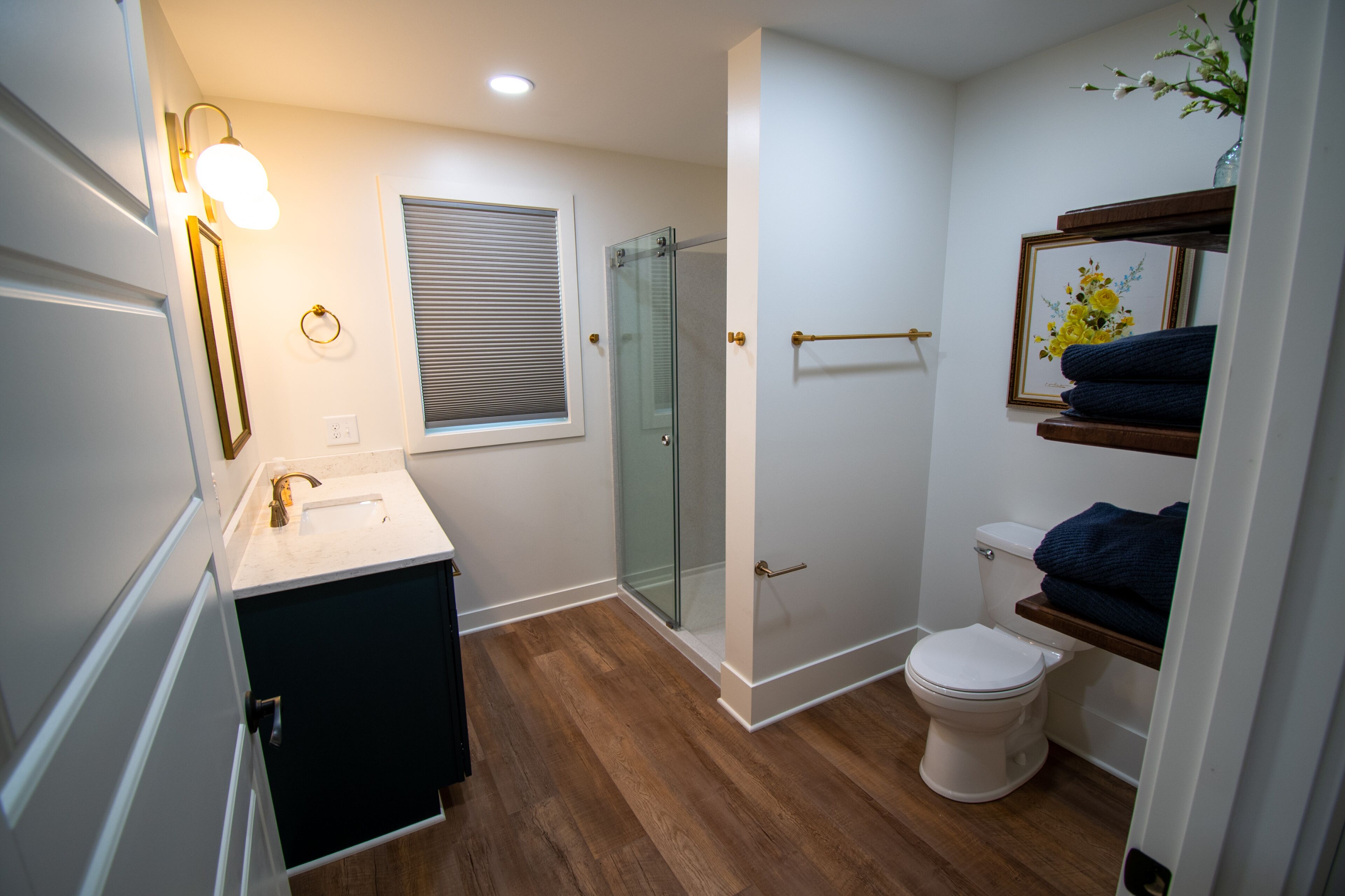 Une salle de bain moderne avec une douche à parois de verre, des toilettes blanches et un meuble-lavabo doté d’un miroir et d’un luminaire.