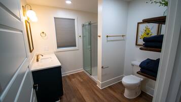 Une salle de bain moderne avec une douche à parois de verre, des toilettes blanches et un meuble-lavabo doté d’un miroir et d’un luminaire.