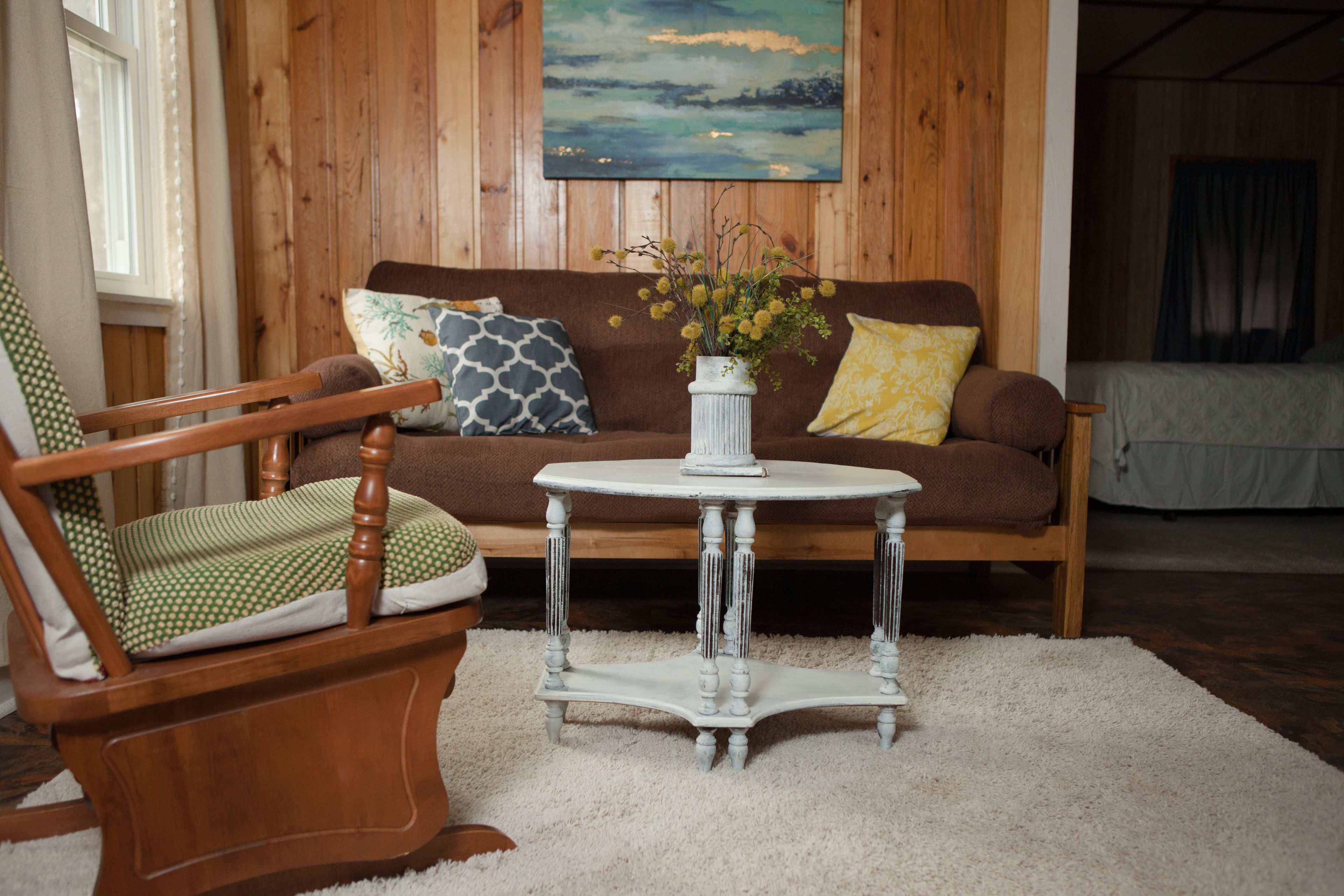 A wooden-furnished living room with a brown sofa, a white round table, and a green and white patterned chair.